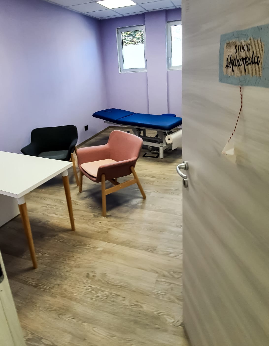 Foto dello studio di ortopedia. All'interno si trovano un tavolo con due poltrone e in fondo un lettino fisioterapico.